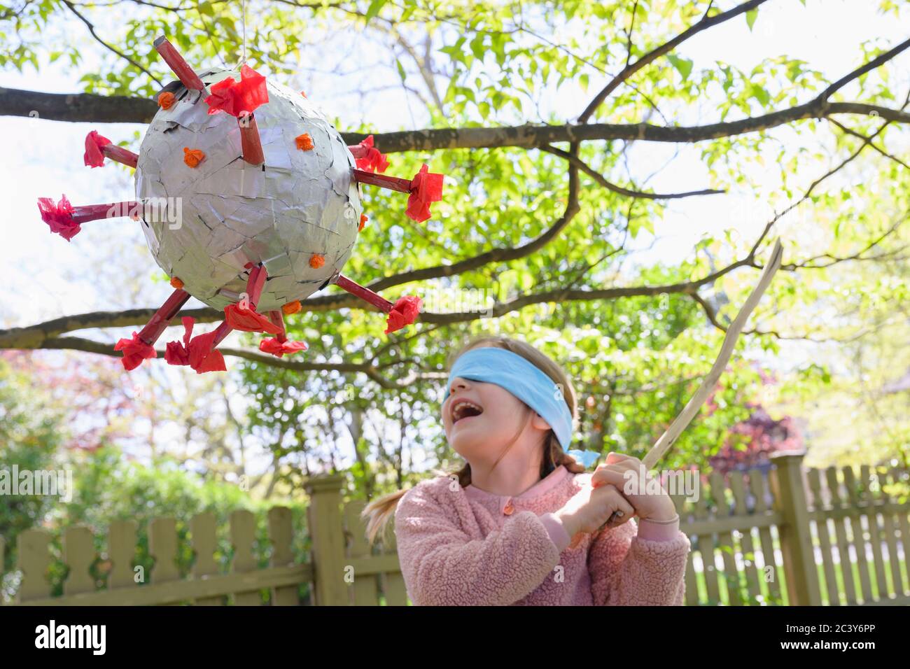 Girl (6-7) hitting coronavirus shaped pinata Stock Photo