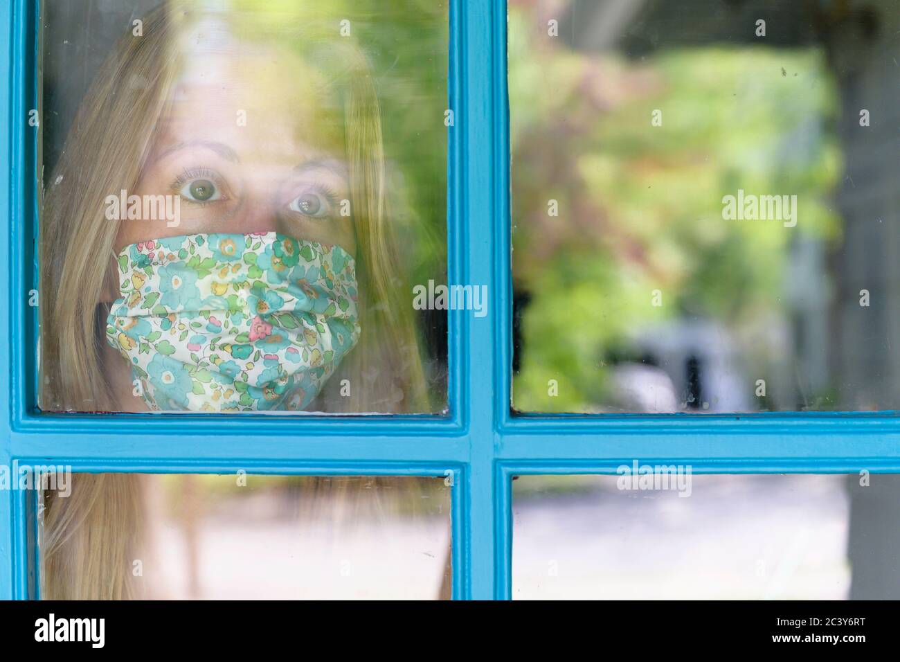 Woman in face mask looking through window Stock Photo