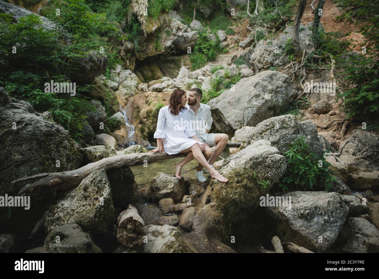 Ukraine, Crimea, Young couple sitting on branch over river in canyon Stock Photo