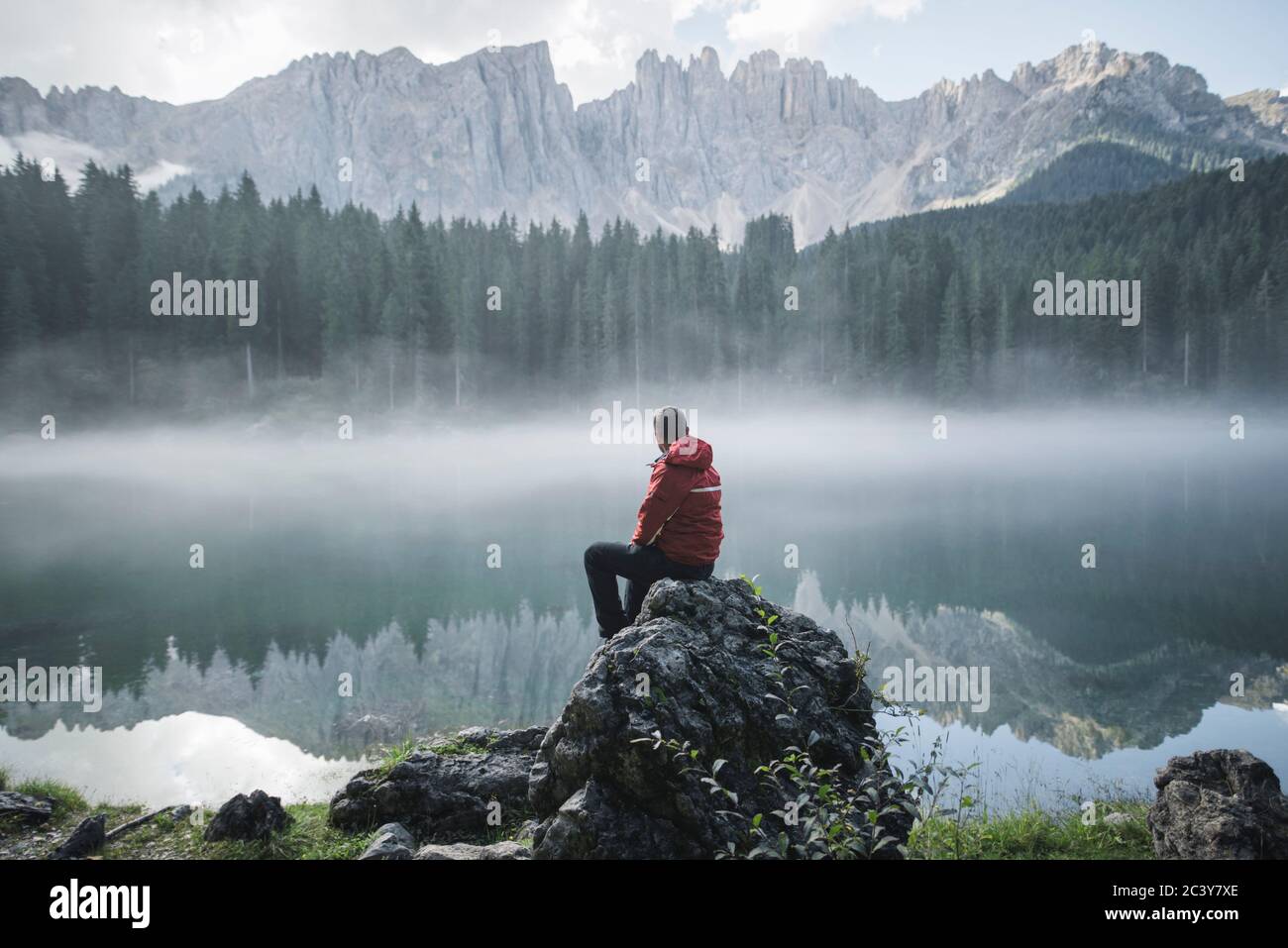 Switzerland, Young man sitting at Lago di Carezza in Dolomite Alps at dawn Stock Photo