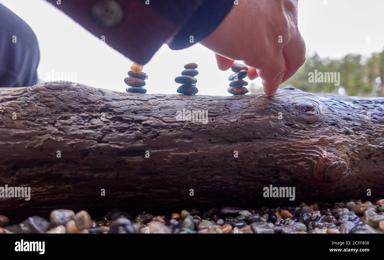 Orcas Island, Man arranging pebble sculpture on log Stock Photo