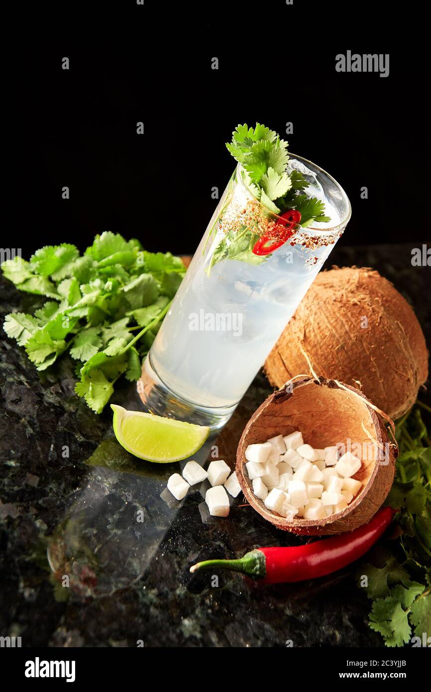 Cocktail with rum, coconut syrup, cilantro, lime and red chilli pepper on black marble bar counter Stock Photo