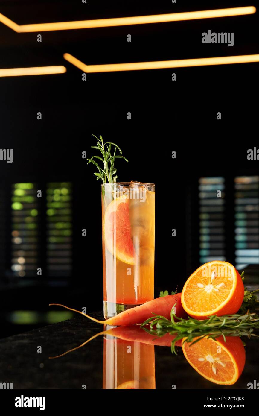 Cocktail with gin, carrot liquor, tonic, orange and rosemary and tonic on black marble bar counter Stock Photo