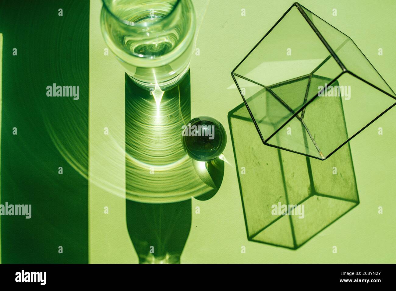 Green lit glass cube, bottle, steel sphere casting disproportionate shadows Stock Photo