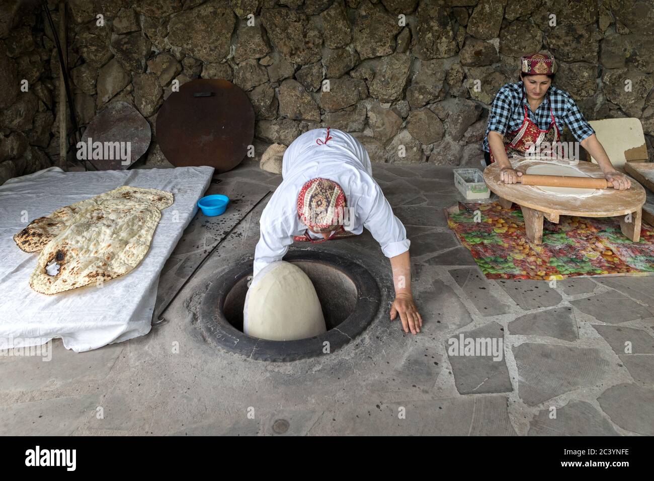 Women preparing Lavash (Armenian Unleavened Flatbread) part of the staple diet, rolling out and slapping to side of hot clay oven with cushion, Yereva Stock Photo