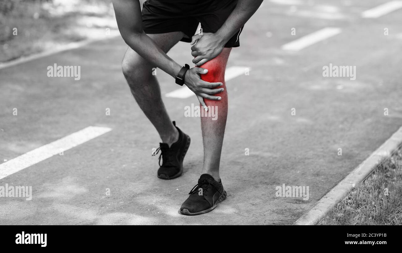Closeup of young sportsman feeling knee pain on jogging track, black