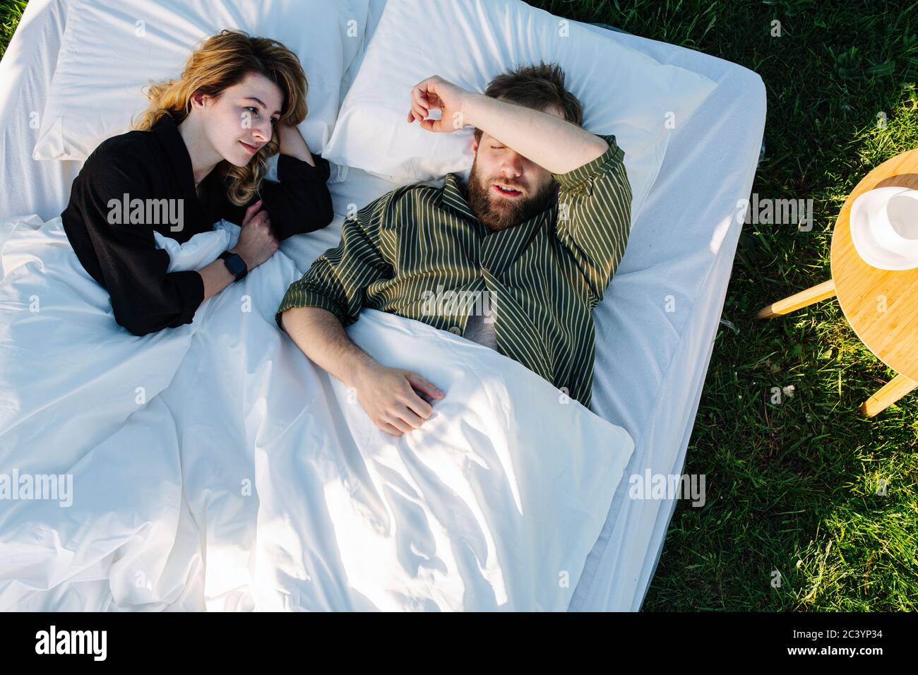 Couple resting on bed made outside on a grass. Wife watching her man