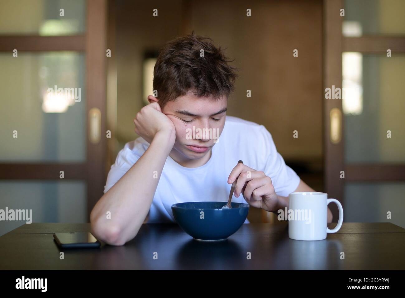 A sleepy teenager lazily eats porridge early in the morning Stock Photo