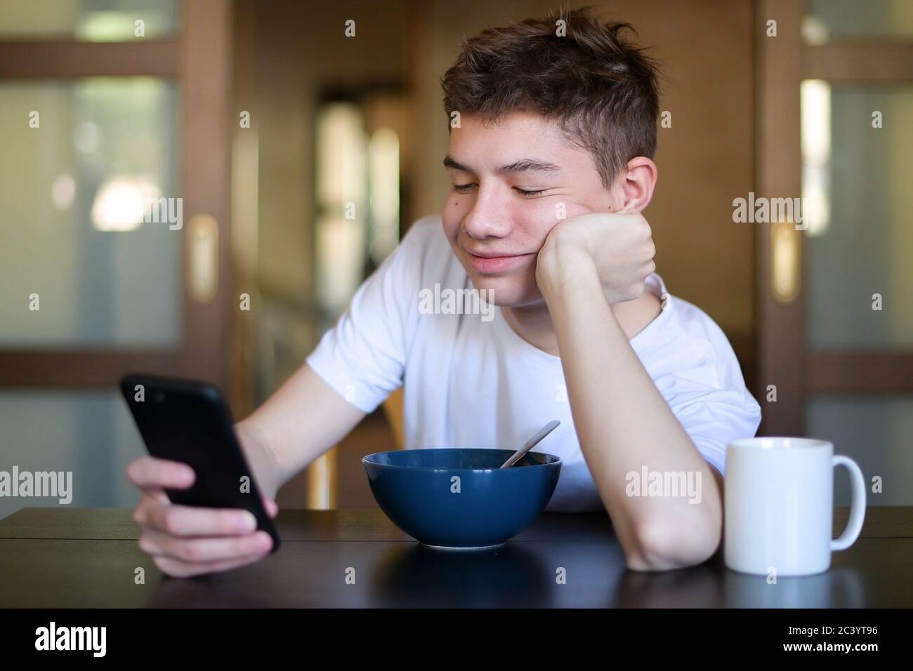 teenager is texting on a smartphone over a plate of porridge during breakfast Stock Photo