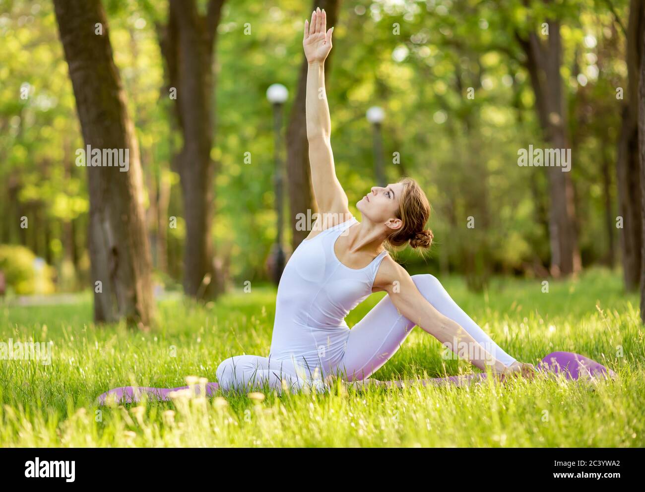 Young female doing yoga stretch and exercise on grass in the park