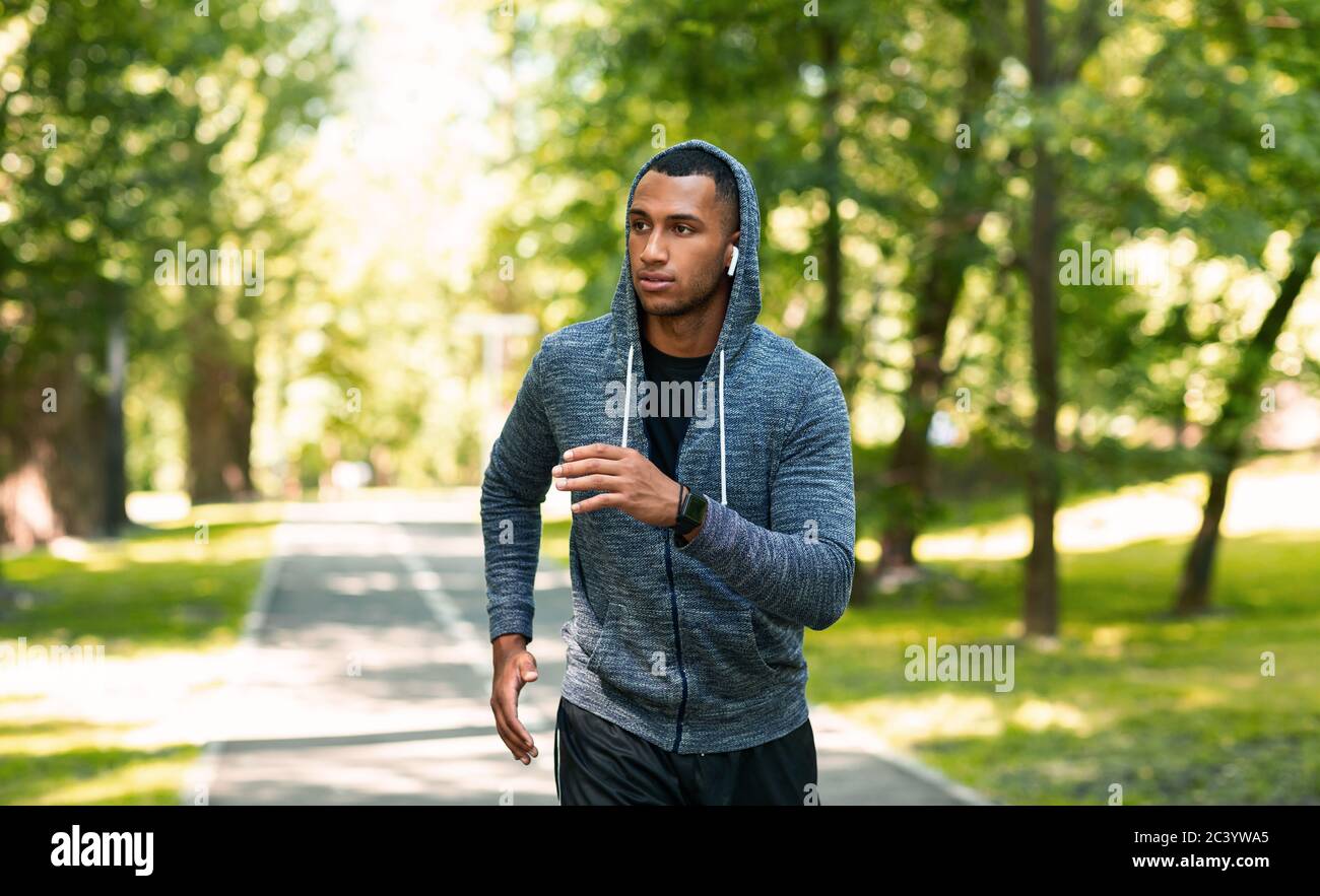 Millennial jogger with earphones enjoying his morning run at summer park, empty space Stock Photo