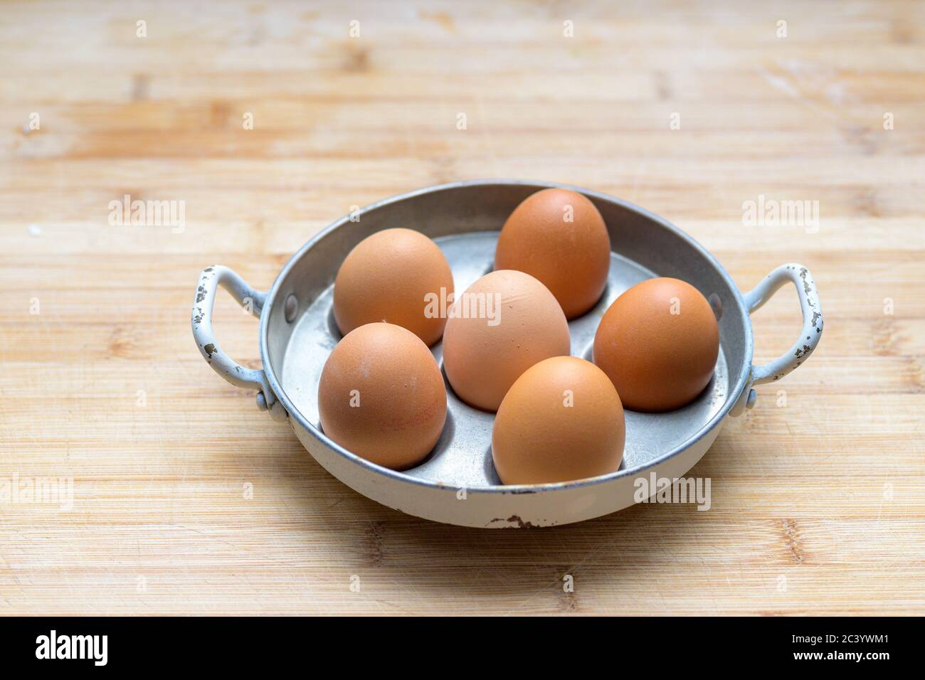 Six fresh brown hens eggs in a metal pot or egg coddler viewed from side on a wooden table with copyspace placed in the centre Stock Photo