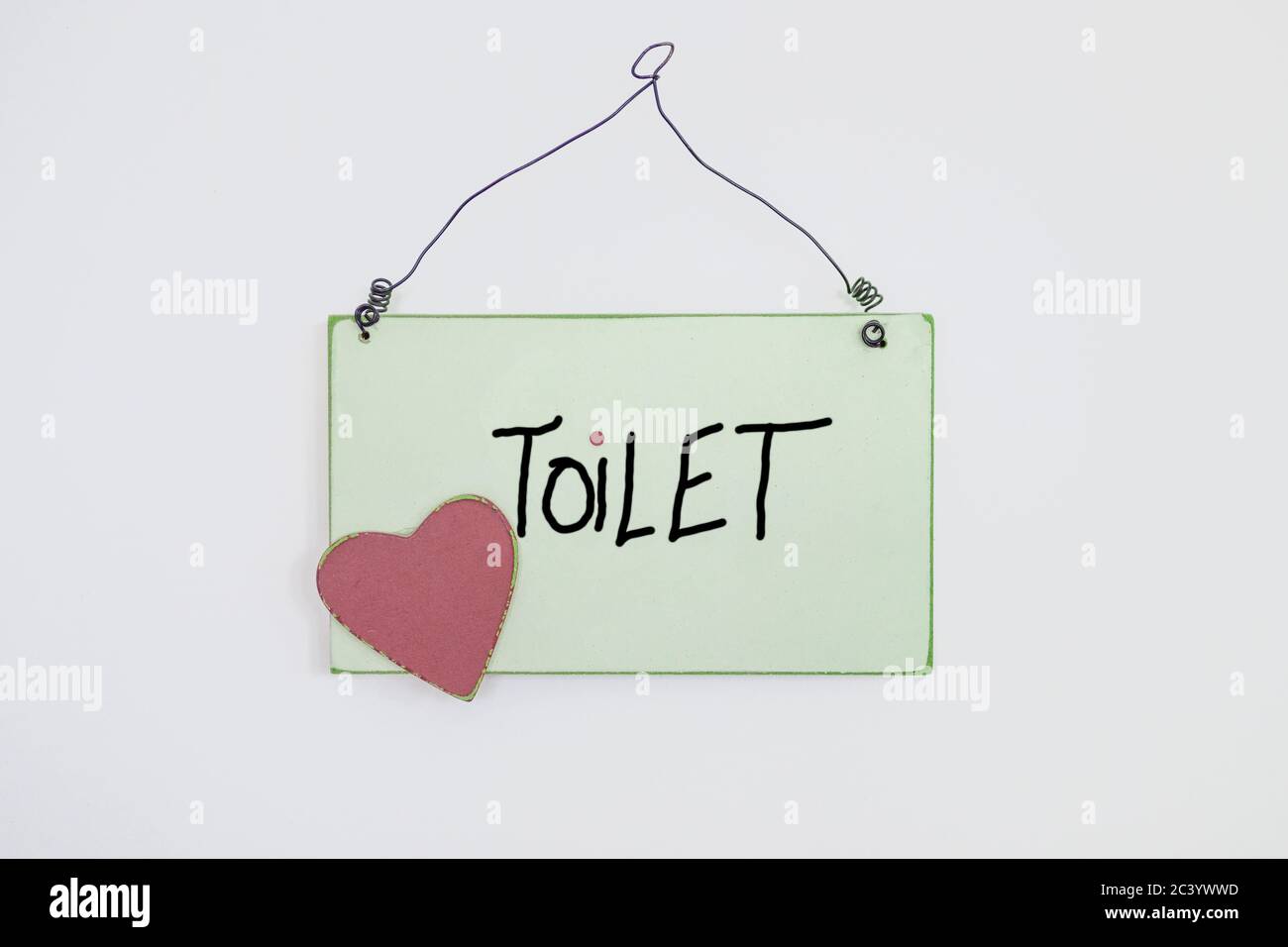 Handwritten Toilet sign with red heart and wire hanger on a white background placed in the centre of the frame Stock Photo