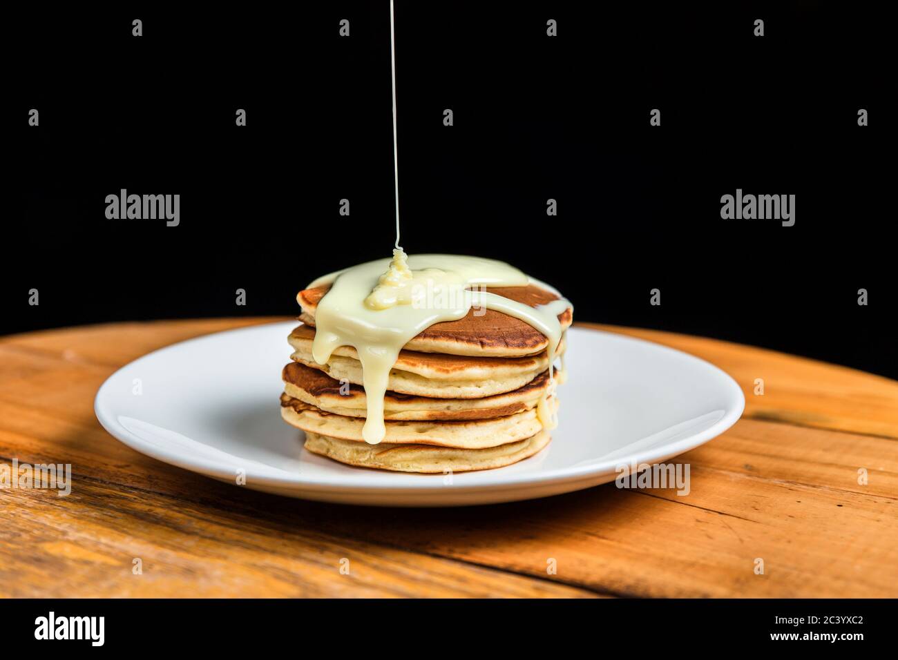 A stack of pancakes with condensed milk on a white plate Stock Photo