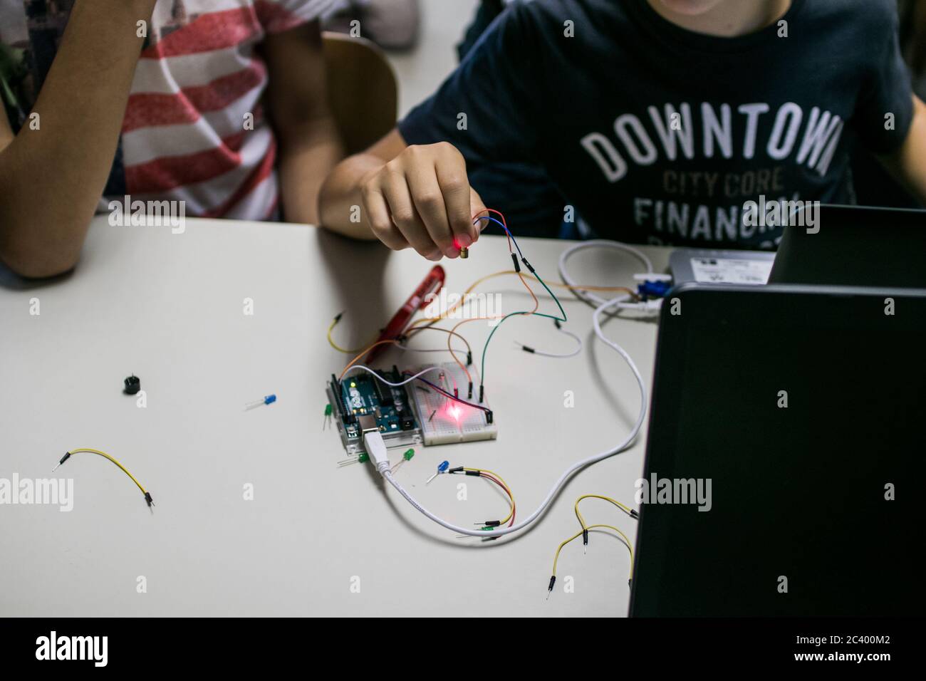 two children build a prototype circuit with a red laser controlled by a microcontroller. STEAM and coding activity Stock Photo