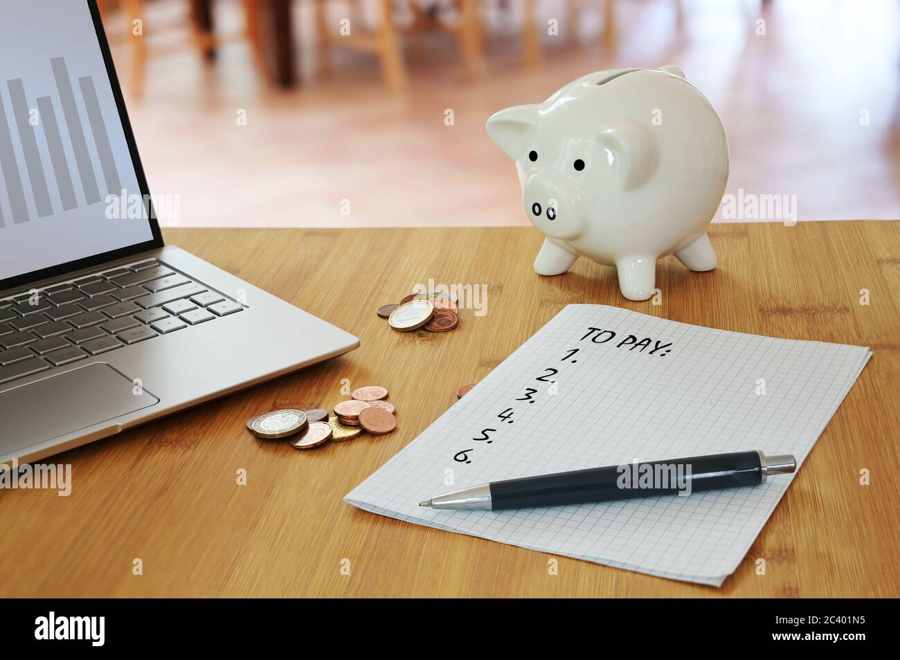 Calculating household costs, laptop, coins, a piggy bank and a list what to pay on a table in the living room, economy finance concept to save money, Stock Photo