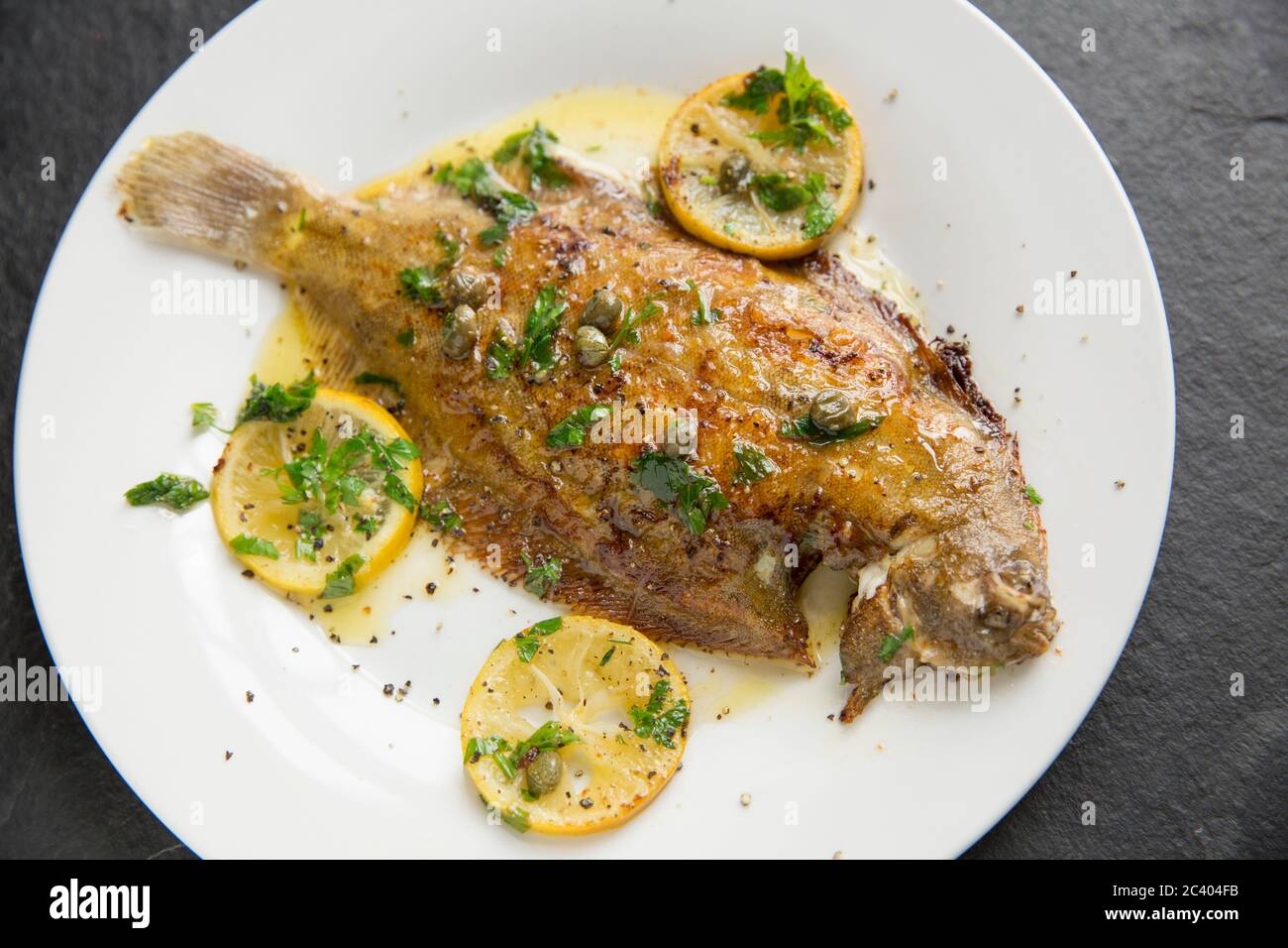 A home cooked whole lemon sole, Microstomus kitt, that has been pan fried in butter with lemon slices, capers and parsley. Presented on a white plate Stock Photo