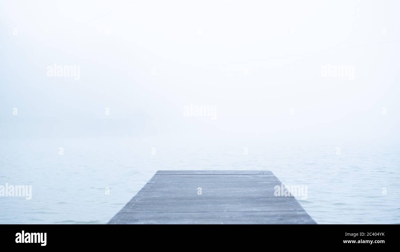 Concept of lonely wooden abandoned dock in fog. Sad and calm mood background. Mist and alone pier. Wallpaper Stock Photo