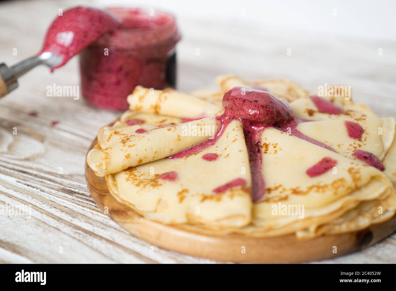 Breakfast with hot pancakes and strawberry ice-cream. Delicate and delicious pancakes on a wooden plate with red jam Stock Photo