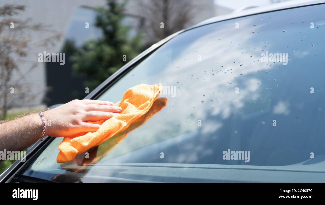 Hand wiping the windshield of a car on a sunny day. Wipe dry with