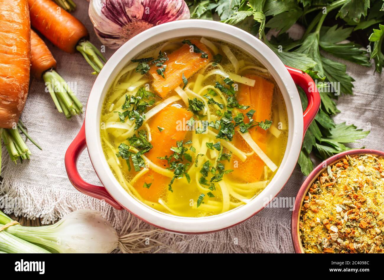 Chicken soup broth in a vintage bowl with homemade noodles carrot onion celery herbs garlic and fresh vegetables. Stock Photo