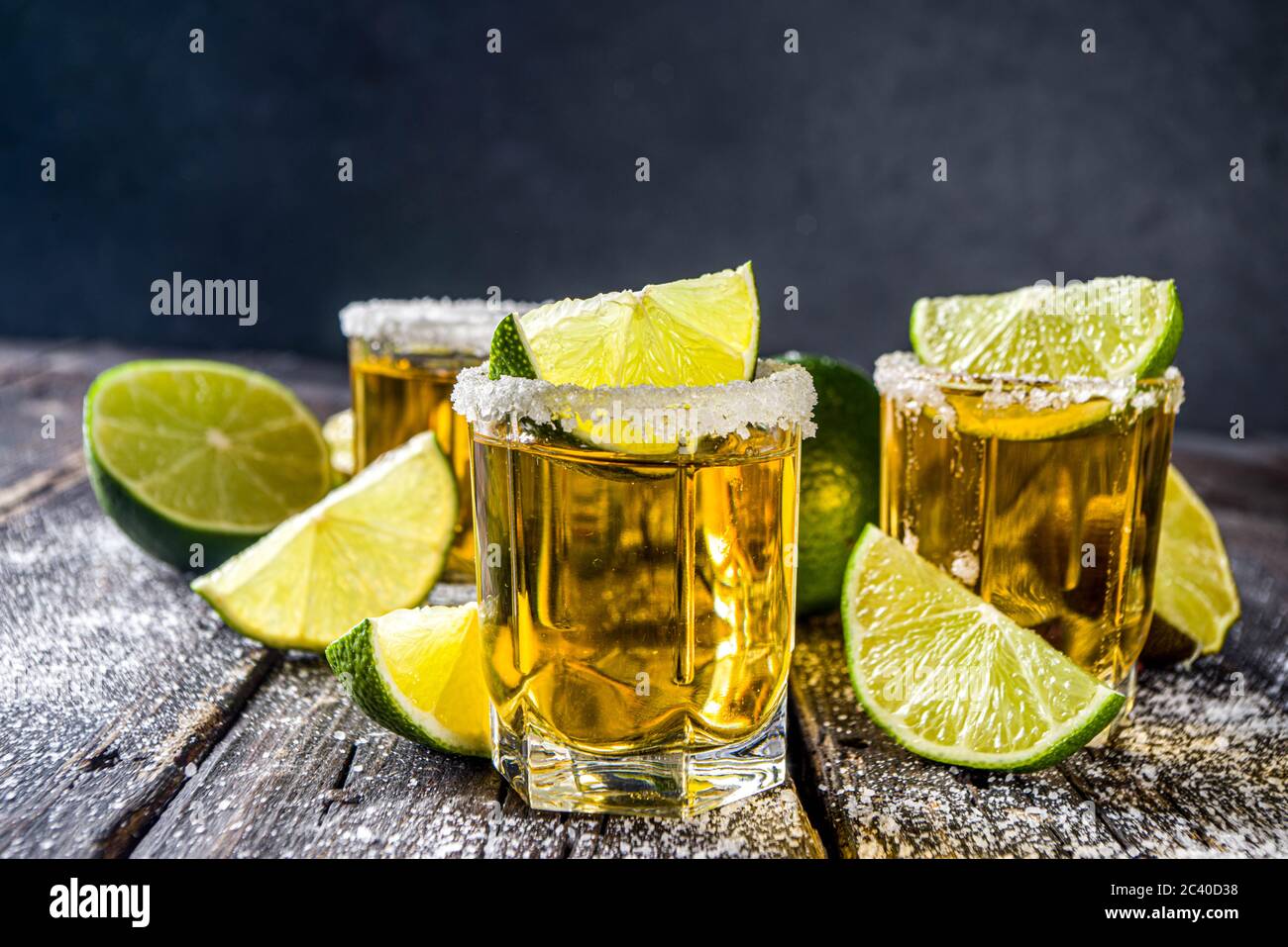 Golden tequila shots. Three tequila shot glasses with salt and lime slices, on wooden background