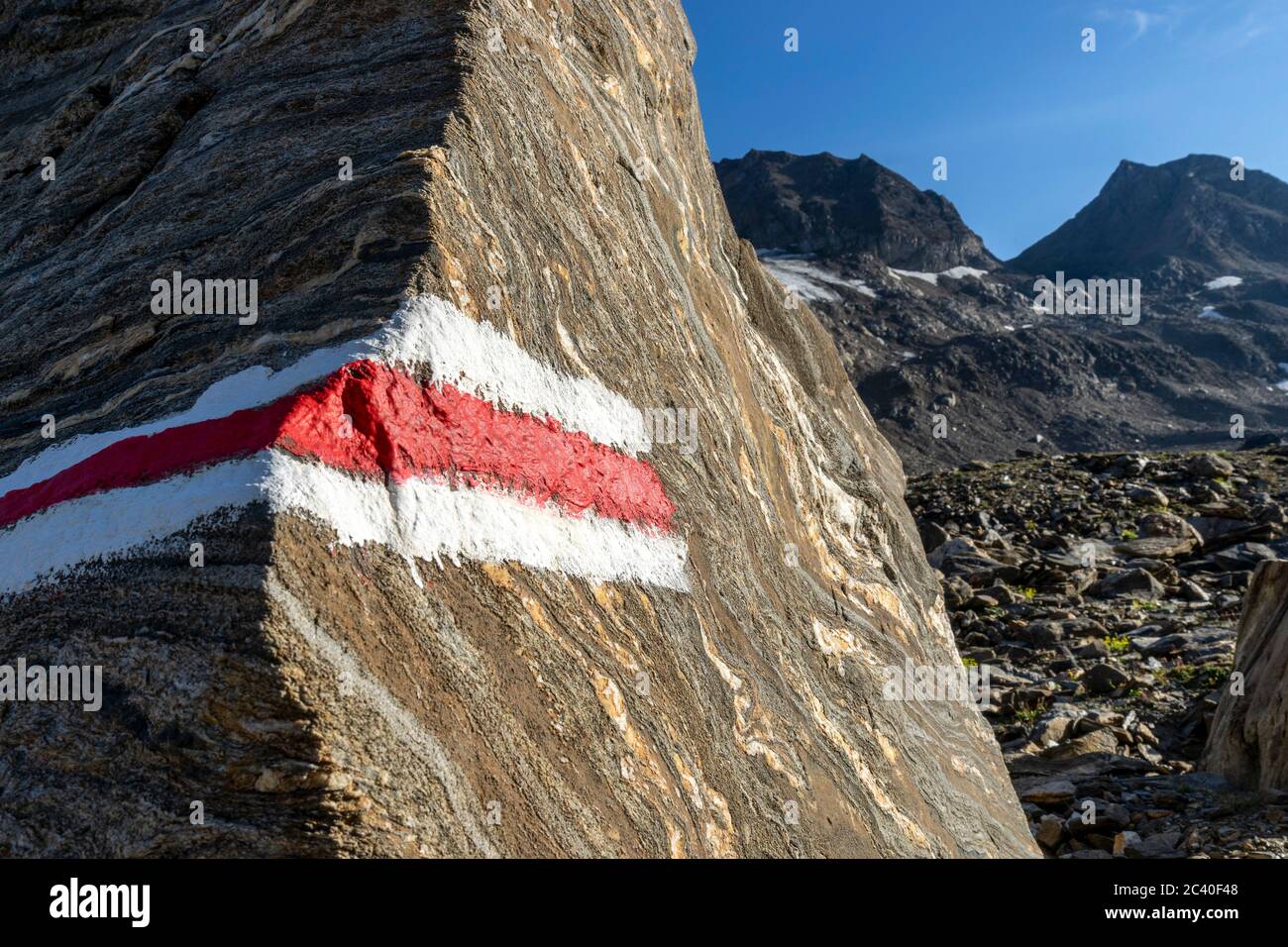 Farbmarkierung eines Bergwanderwegs auf einem gebänderten Felsblock im Val Corno, Kanton Tessin. Links hinten das Klein Grieshorn oder Piccolo Corno G Stock Photo