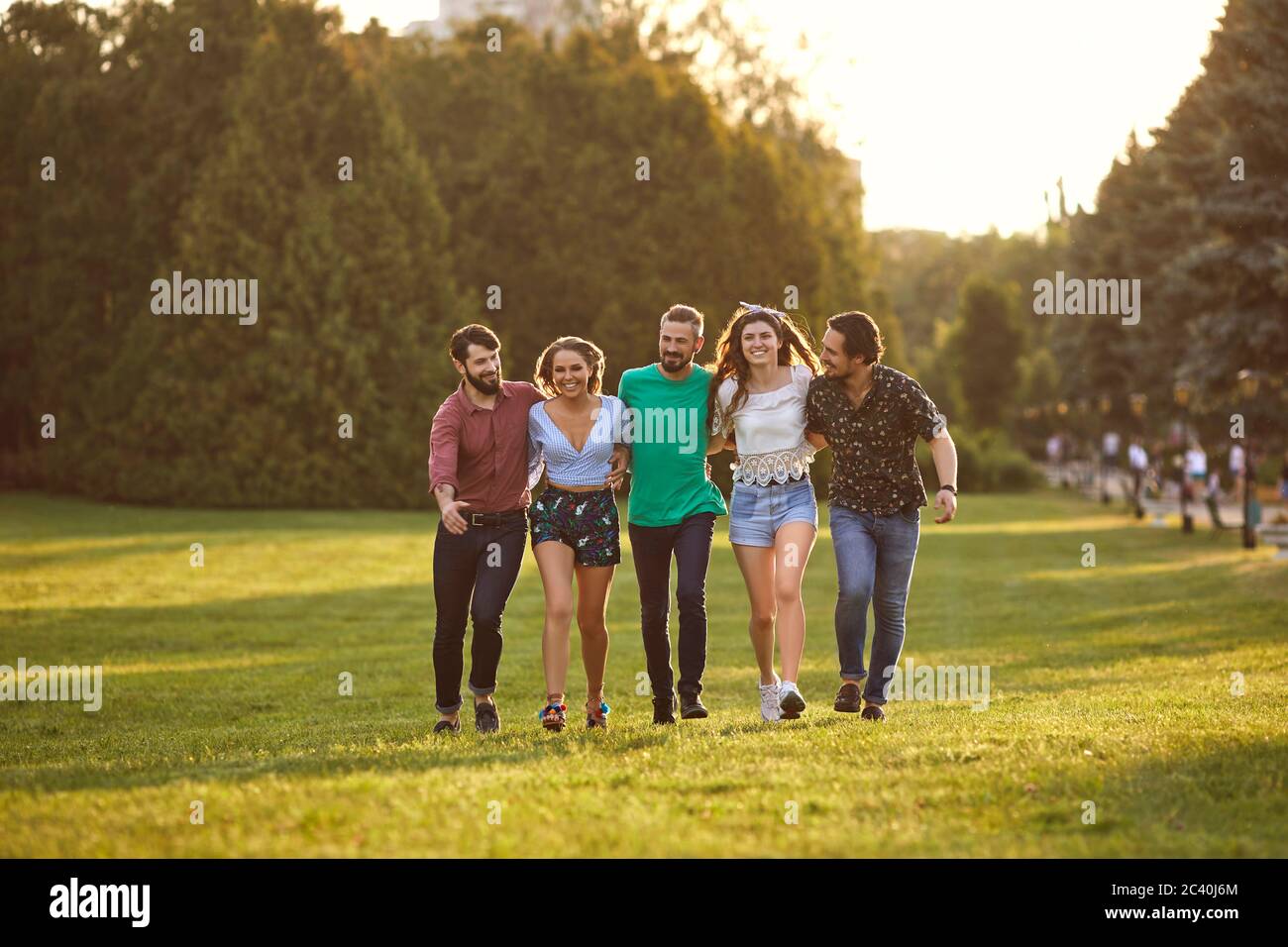 A group of friends have fun walking on the grass in the summer park. Stock Photo