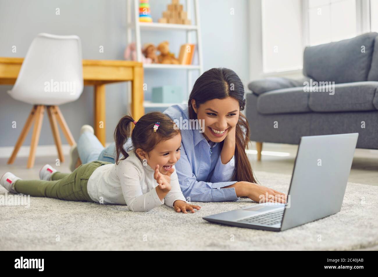 Mom with her daughter watching cartoons or entertainment video online at home. Parent and child with laptop on floor Stock Photo