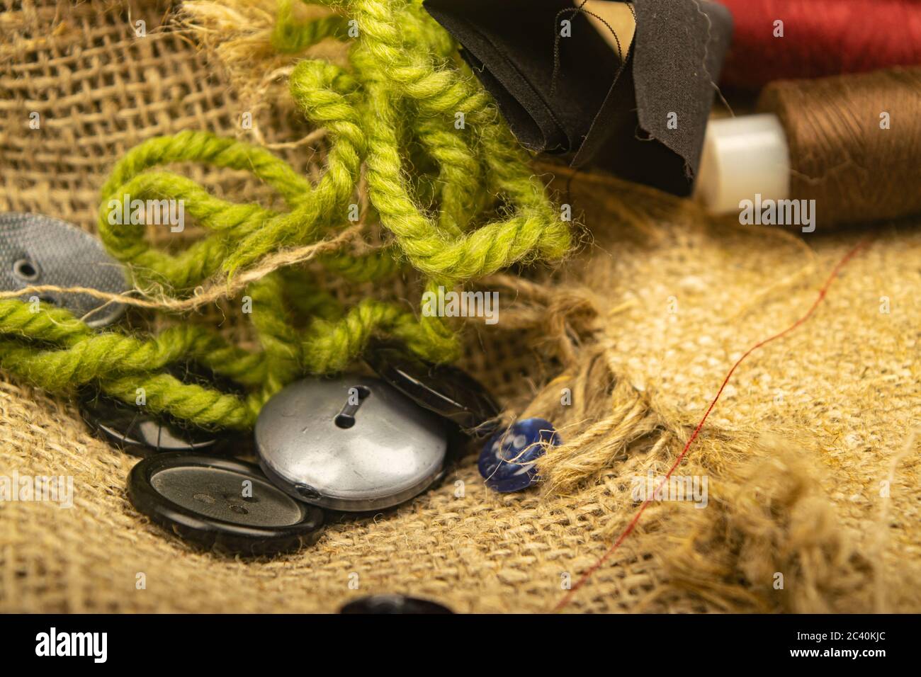Various buttons and multicolored threads on coarse-textured burlap. Close up Stock Photo