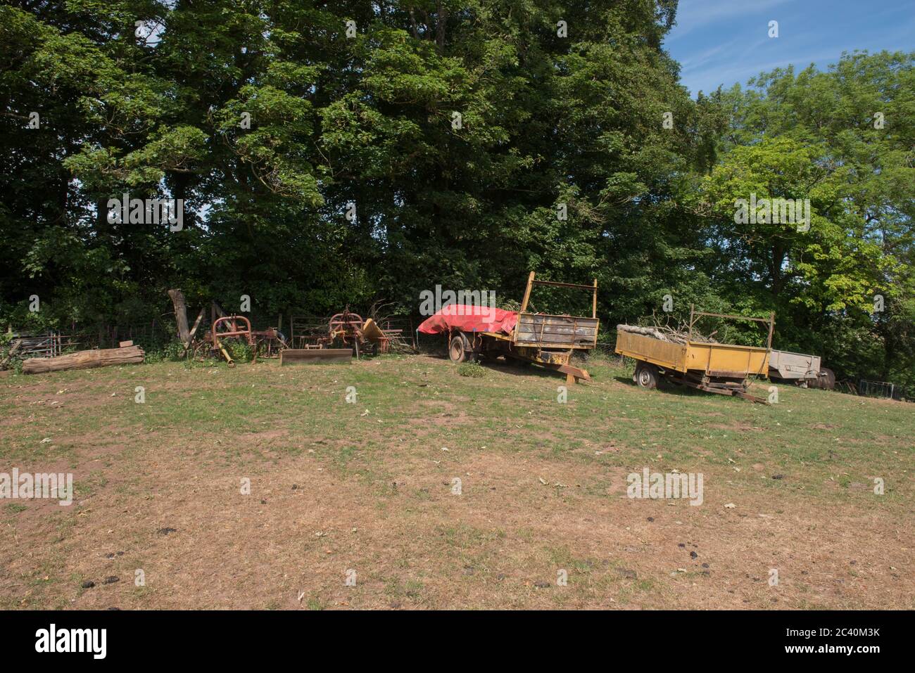 Group of Rusty Old Farm Machinery and Trailers on Top of a Hill in a Field on a Farm in Rural Devon, England, UK Stock Photo