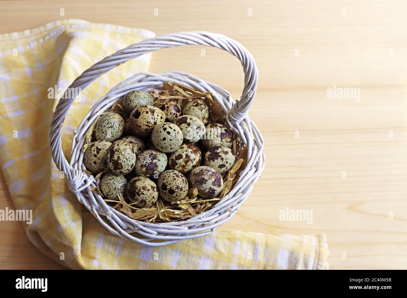 wicker basket with spotted quail eggs standing on a wooden table Stock Photo