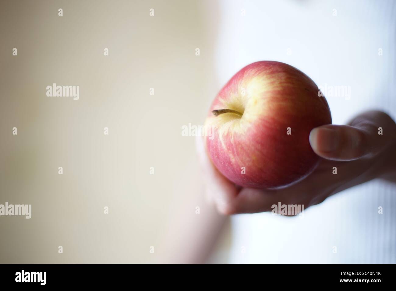 Red apple in female hand on the blurred background. Copy space. Stock Photo