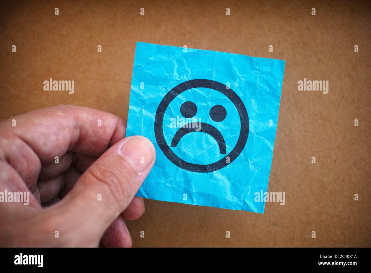 Man holding blue paper note with sad face on it in his hand. Closeup. Stock Photo
