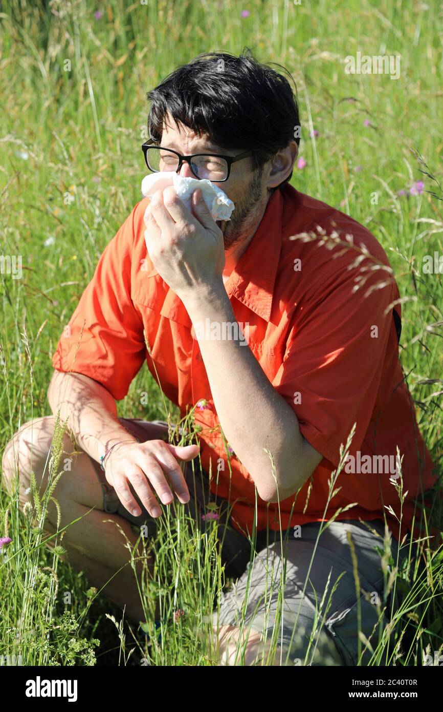 young boy you had and sneezes with a handkerchief because he is allergic to pollen in the middle of the lawn in summer Stock Photo