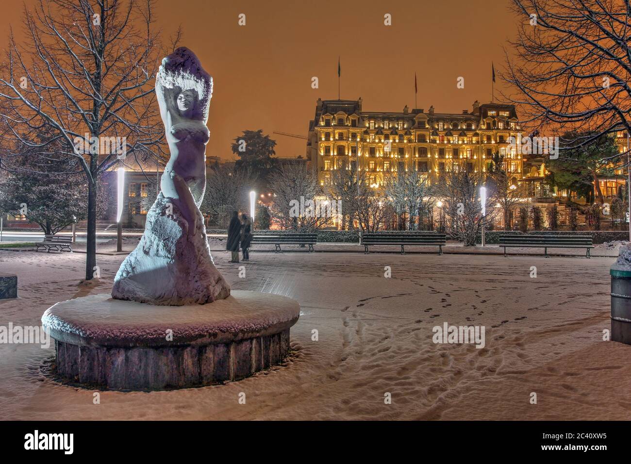 Snowing winter night on the Quai d'Ouchy in Lausanne, Switzerland featuring a statue and one of the luxury hotels in the background. Stock Photo