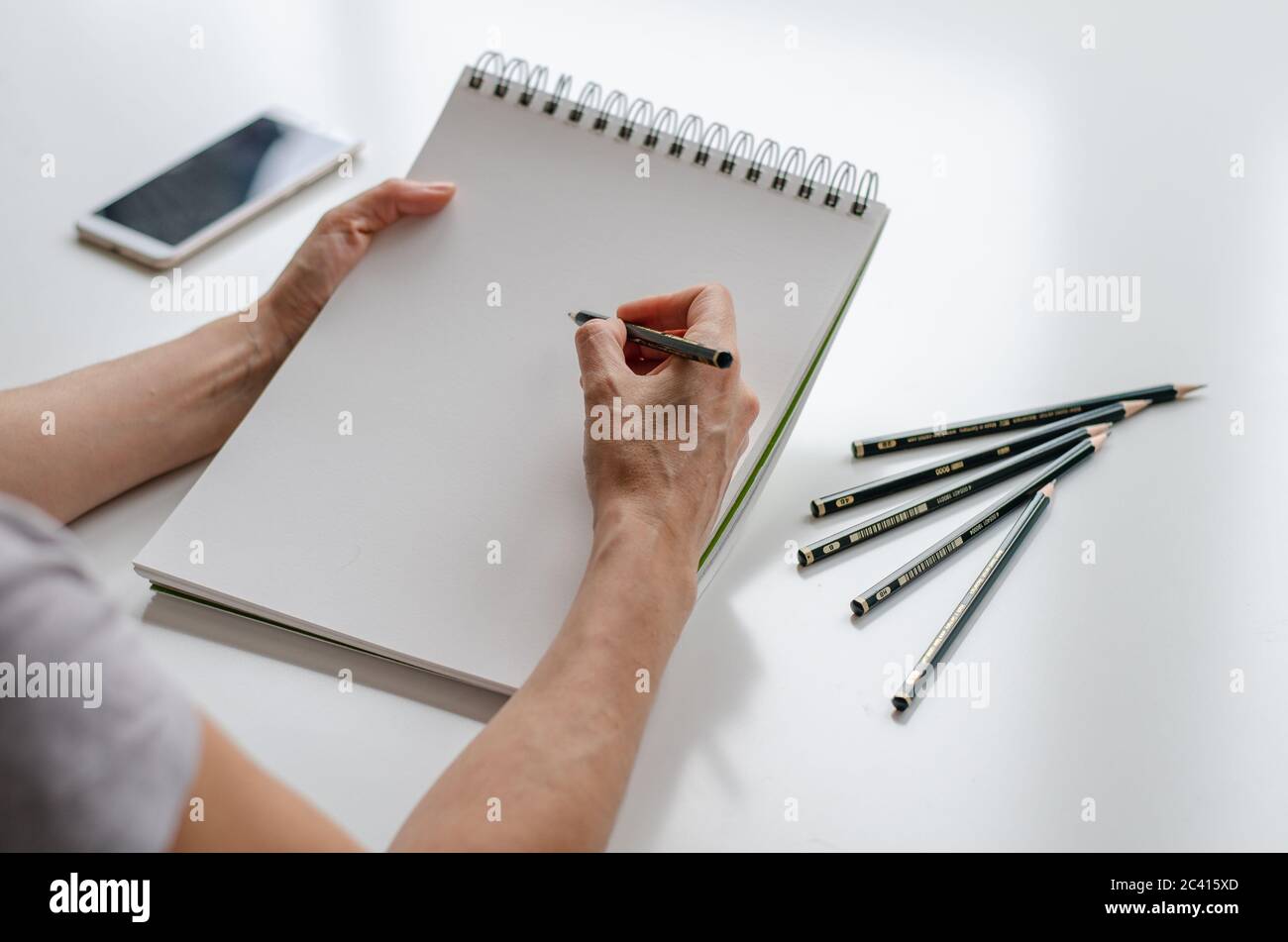Woman drawing in a sketchpad. Close up view. Pencils and cell phone on the table. Right handed Stock Photo