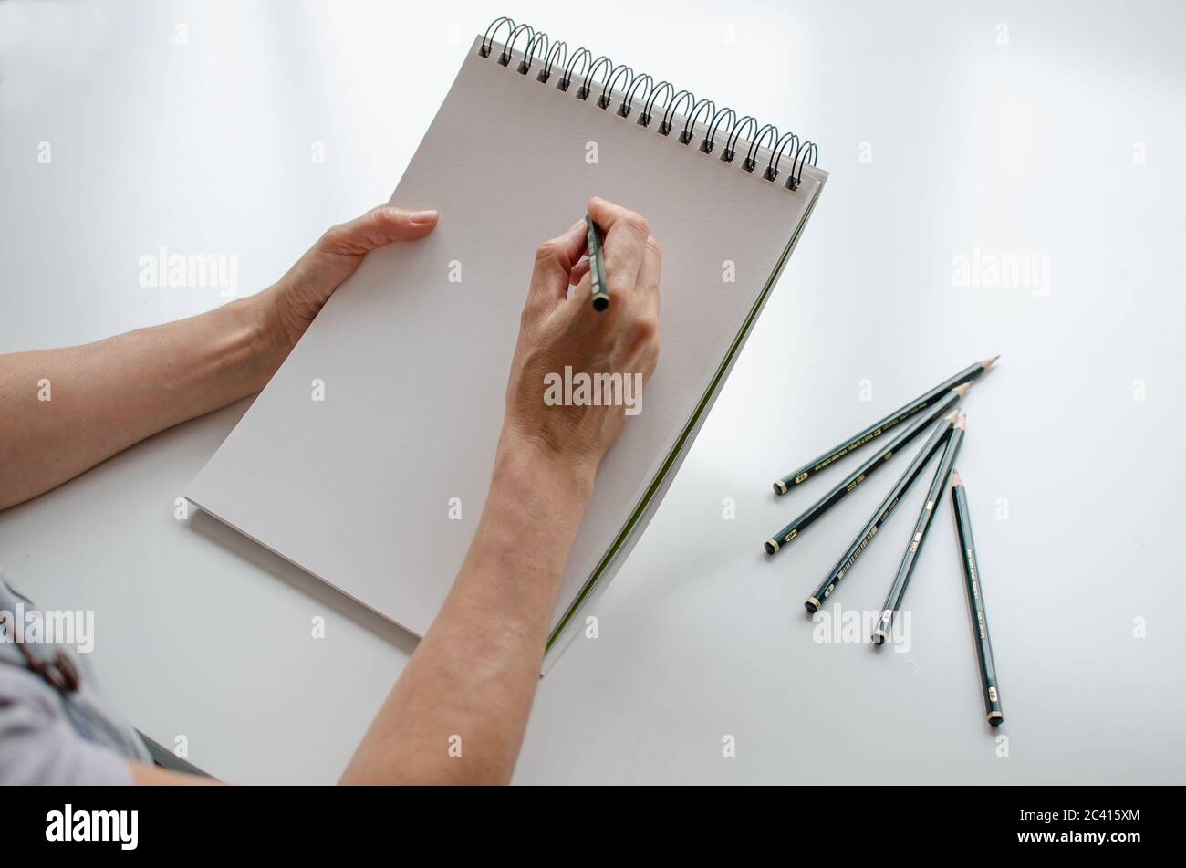 Woman drawing in a sketchpad. Close up view. Pencils on the table. Right handed Stock Photo