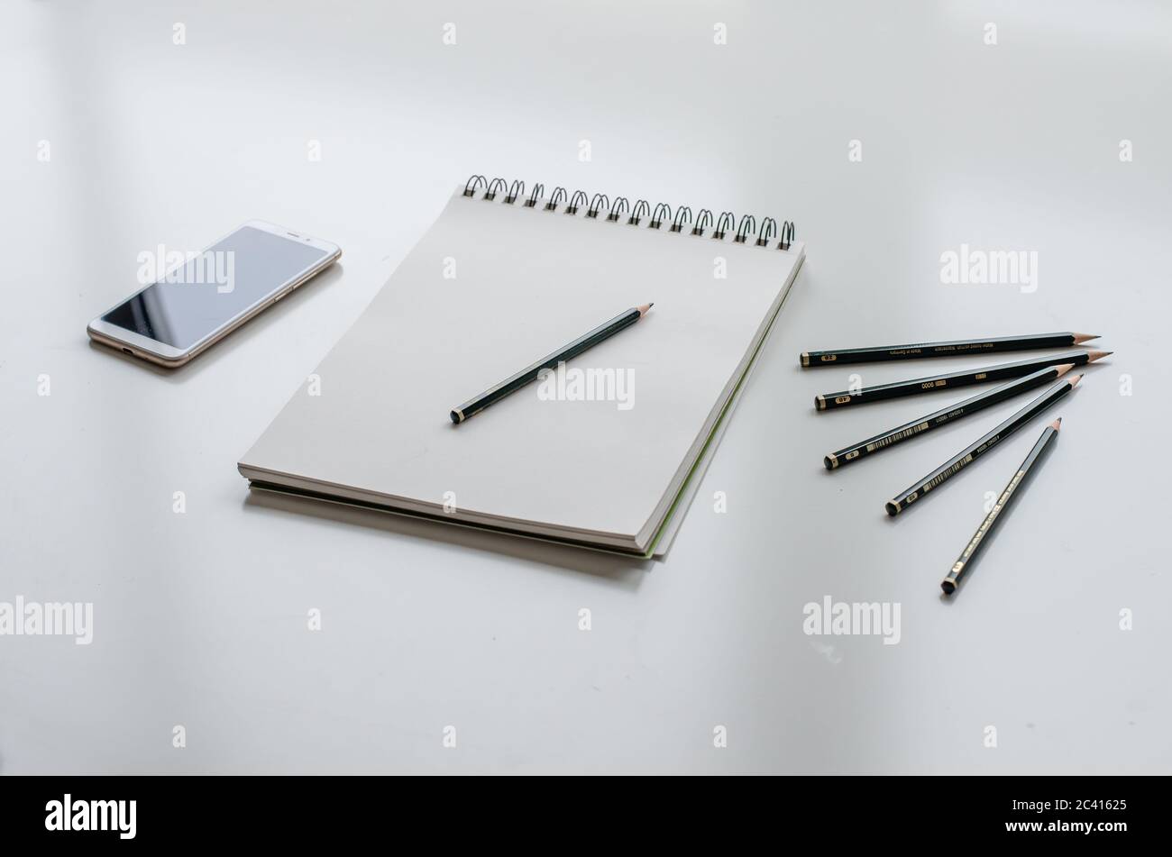 Sketchpad with a pencil. A cell phone and five pencils on a white desk. Stock Photo
