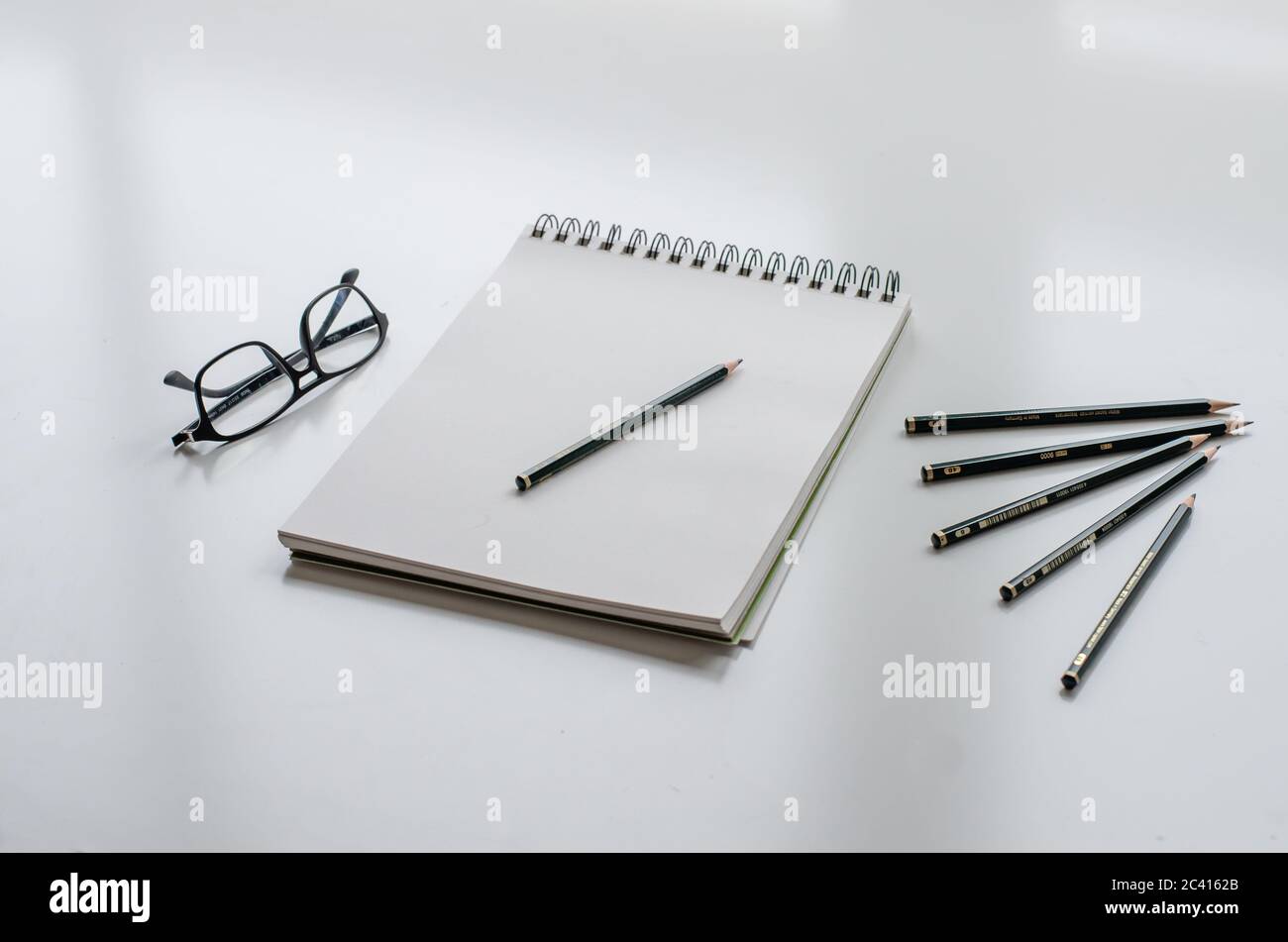 Sketchpad with a pencil. Glasses and five pencils on a white desk. Stock Photo