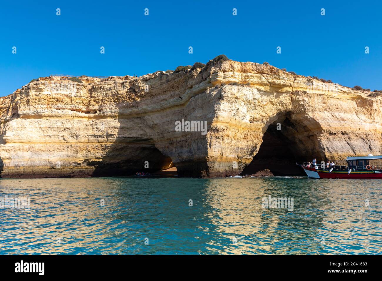 Landscape with the famous Benagil Caves, clear blue sky, sandstone cliffs and tour boat on the Algarve coast in Portugal Stock Photo