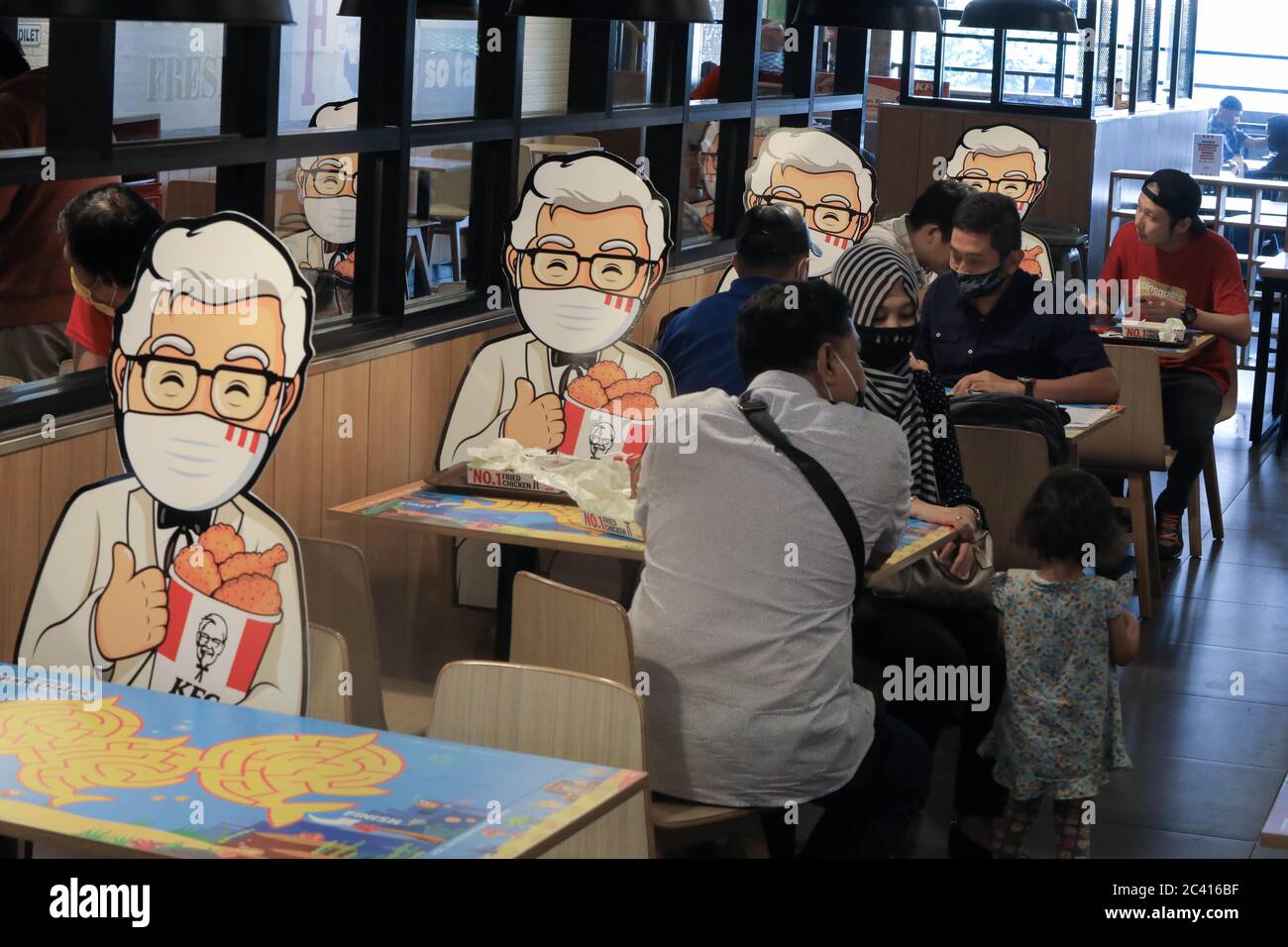 South Jakarta, Indonesia. 23rd June, 2020. Customers sit next to Colonel Sanders' characters mounted at tables as a way of maintaining the social distance, a precaution against the spread of coronavirus (covid-19) at KFC. Credit: SOPA Images Limited/Alamy Live News Stock Photo