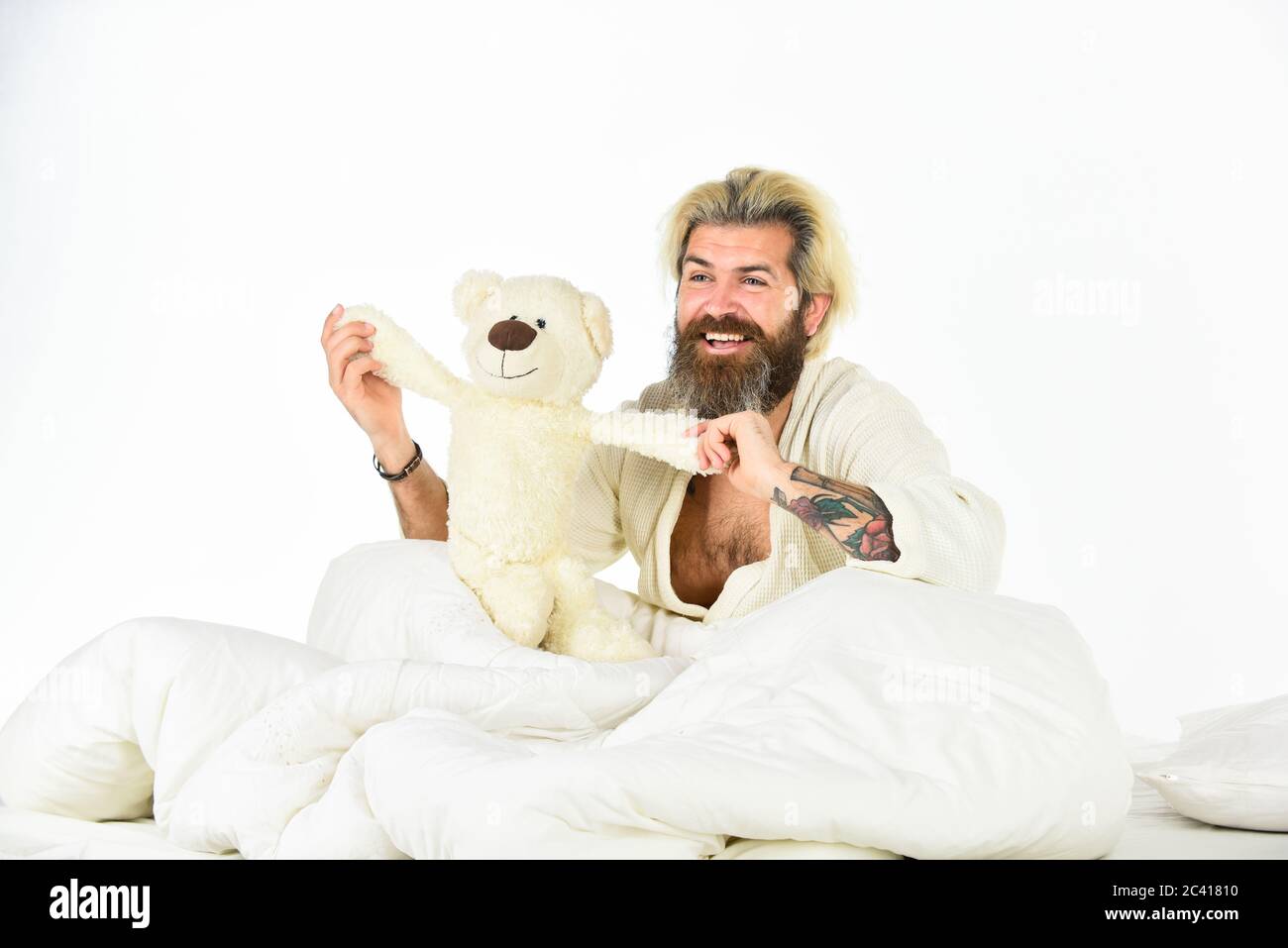 Bearded hipster play toy. Man hug soft toy relaxing in bed. Lovely