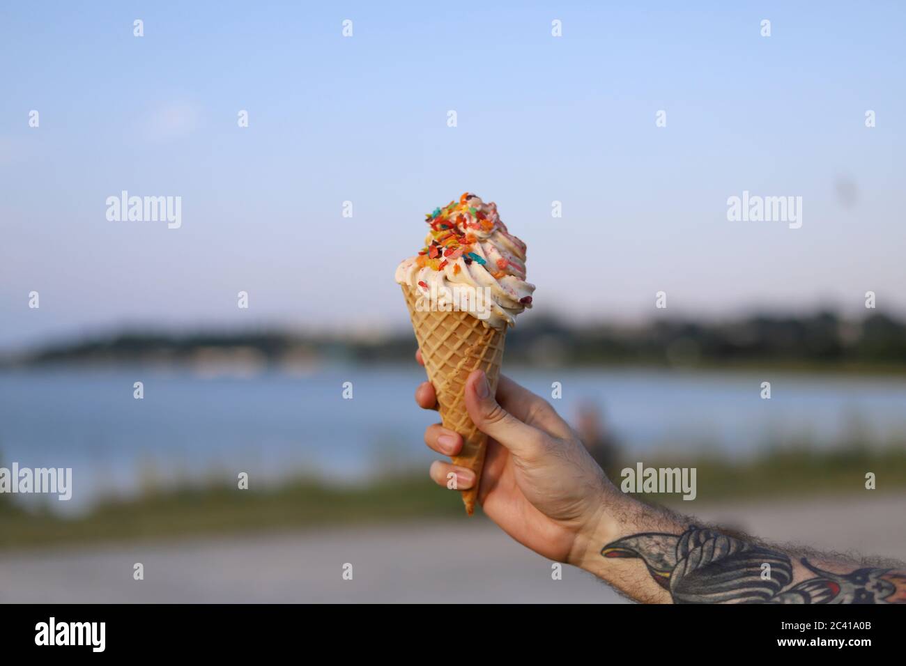 A man's hand holds up a big waffle cone ice cream with sprinkles Stock Photo