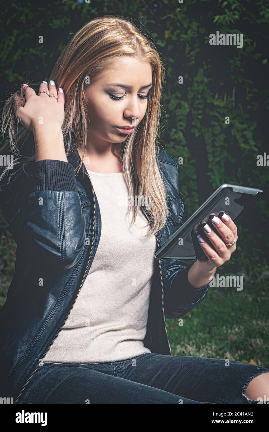 Blond haired studen doing e-learning in the park via her tablet PC. Vintage looking matte style image. Stock Photo