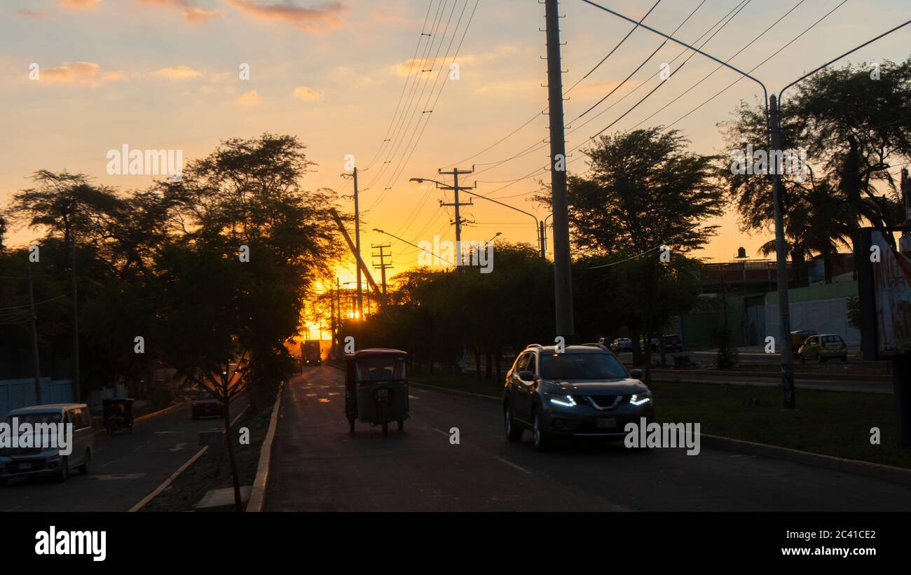 San Miguel de Piura, Piura / Peru - April 5 2019: View of a sunset on a street with trees and cars in black silhouette with the sun hiding among the t Stock Photo