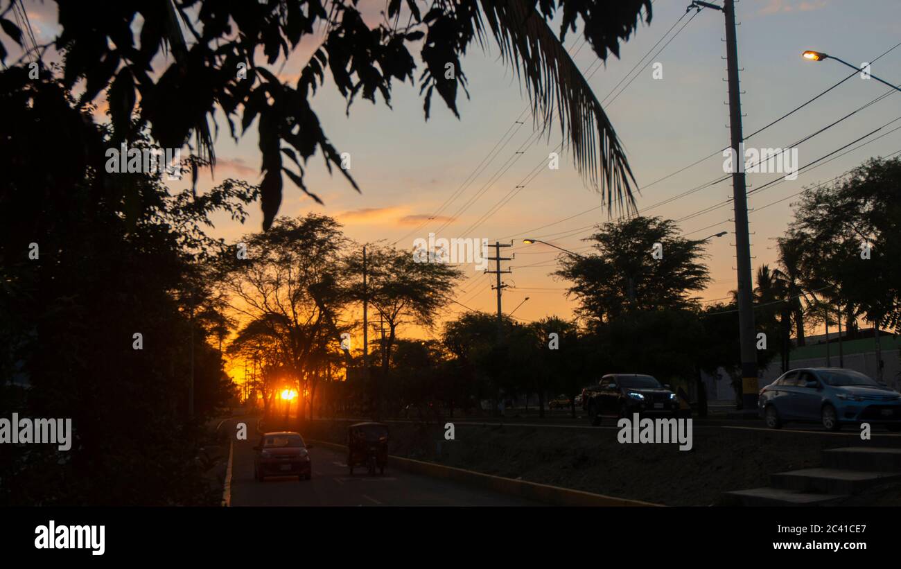 San Miguel de Piura, Piura / Peru - April 5 2019: View of a sunset on a street with trees and cars in black silhouette with the sun hiding among the t Stock Photo