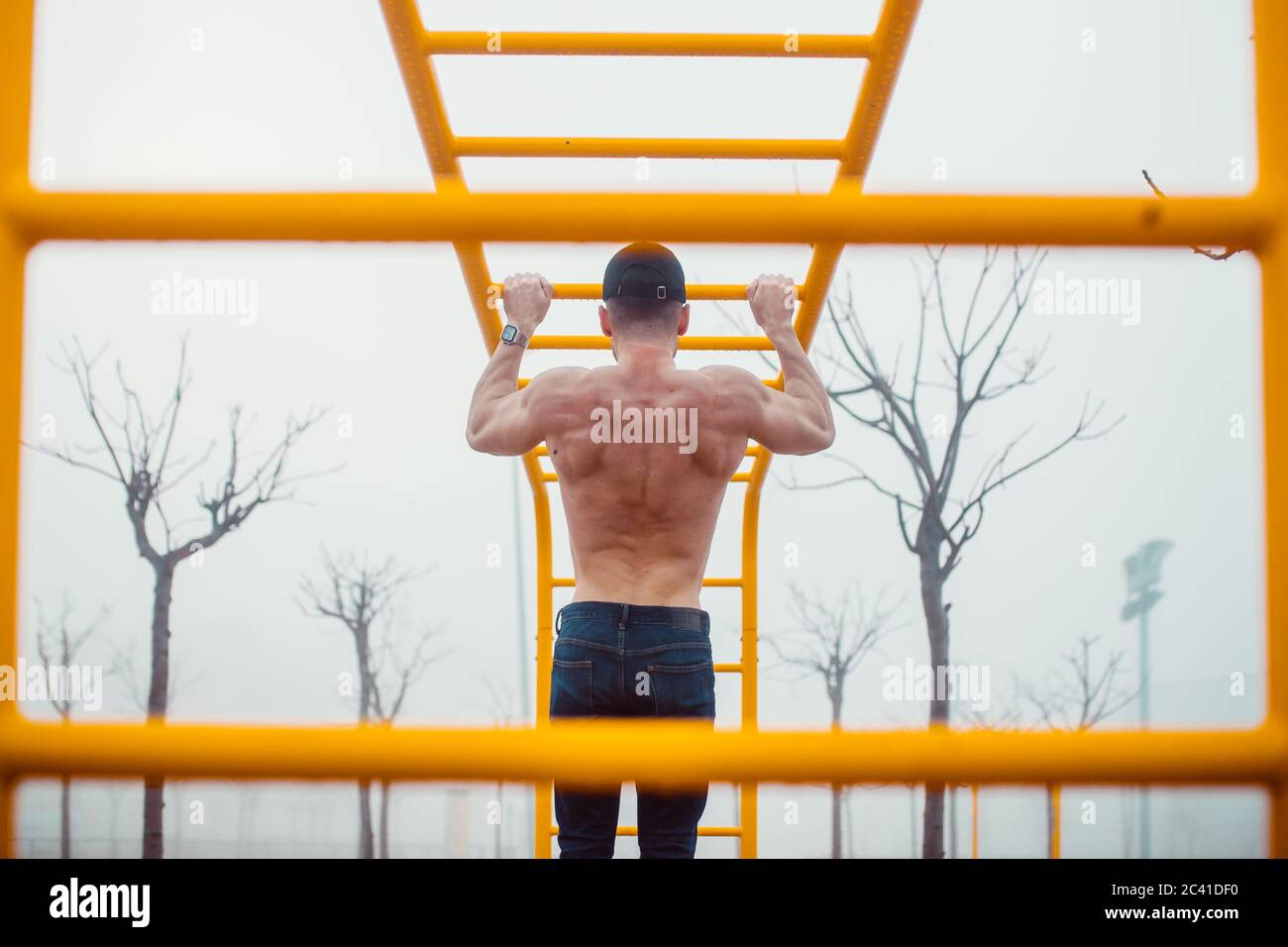 man with cap doing pull-ups in a calisthenics park. back photo Stock Photo