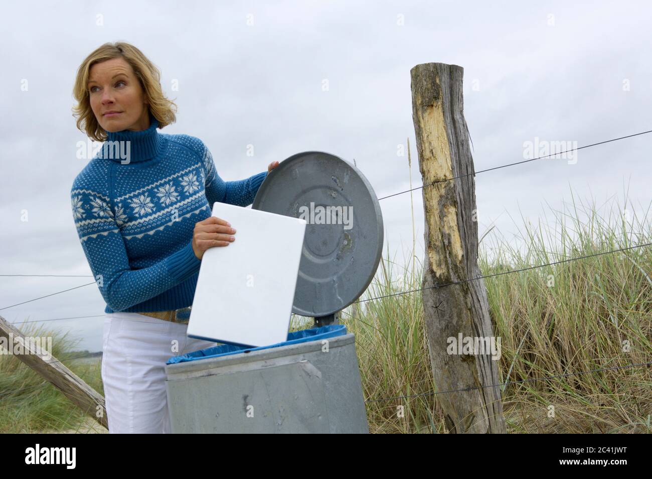 Elderly woman puts laptop in a garbage can Stock Photo