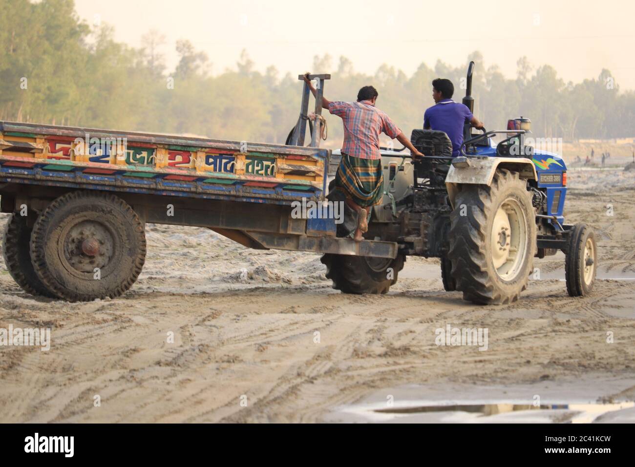 Two workers are lifting sand in the dry river with a tractor trolley. Stock Photo